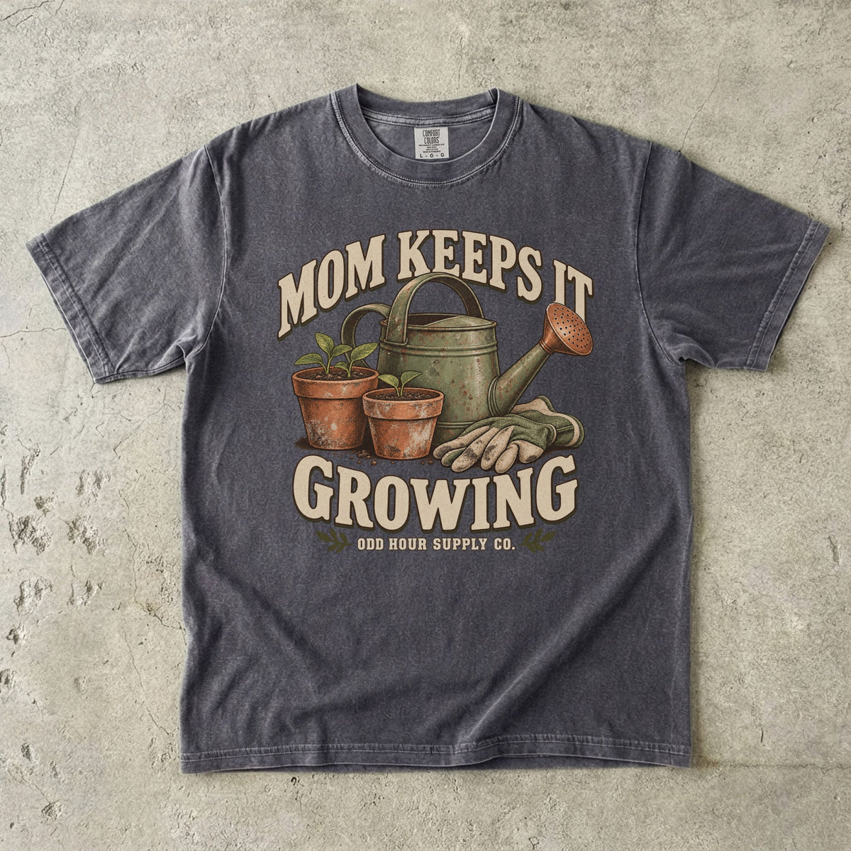 Pepper Comfort Colors 1717 T-shirt with a green watering can, two terracotta pots with seedlings, gardening gloves, and Mom Keeps It Growing lettering.