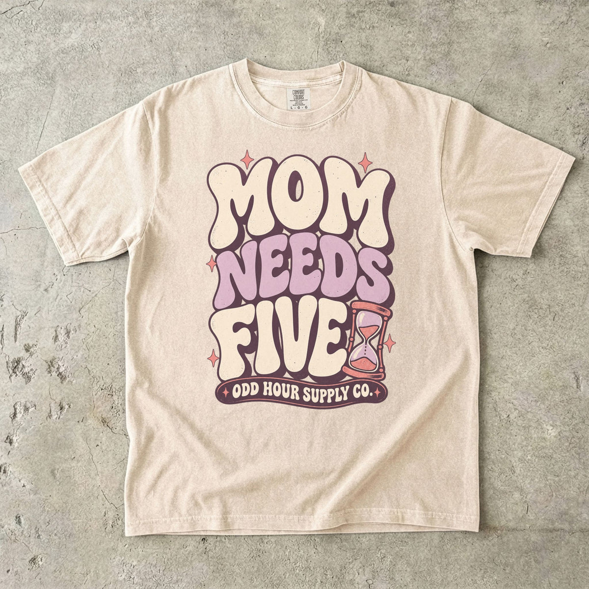 Ivory Comfort Colors 1717 T-shirt with cream and lilac Mom Needs Five lettering, pink stars, and an hourglass.