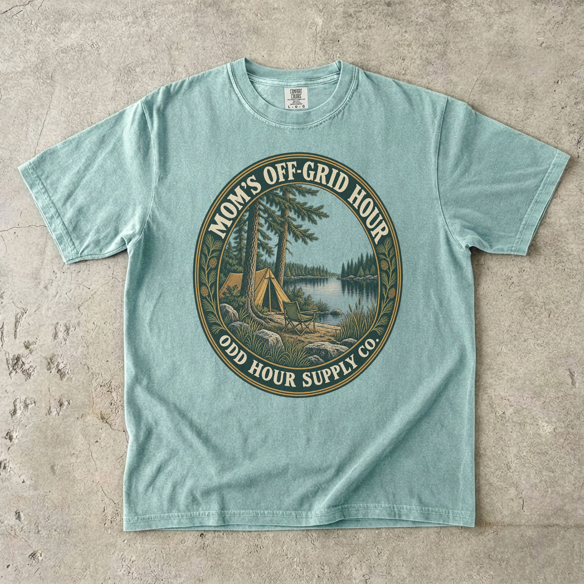 Bay Comfort Colors 1717 T-shirt with an oval Mom’s Off-Grid Hour badge showing a tent, a camp chair, pine trees, and a lake.