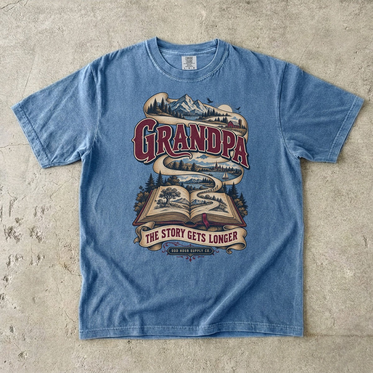 Blue Jean T-shirt with GRANDPA THE STORY GETS LONGER, an open book and a landscape ribbon by Odd Hour Supply Co.