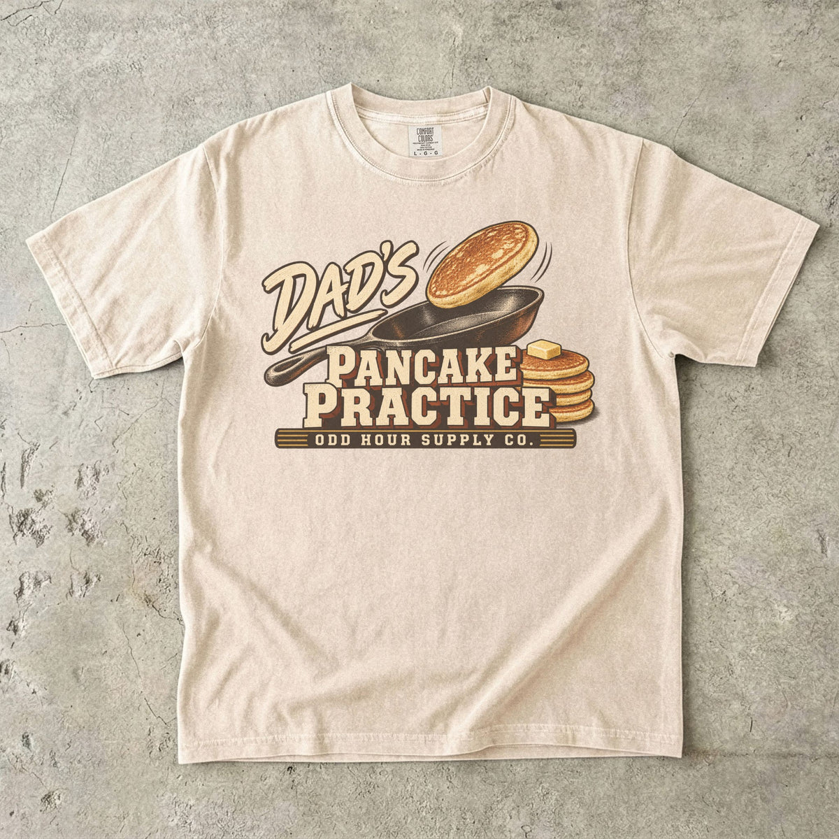 Ivory Comfort Colors 1717 T-shirt with a cast-iron pan, an airborne pancake, a pancake stack with butter, and Dad’s Pancake Practice lettering.