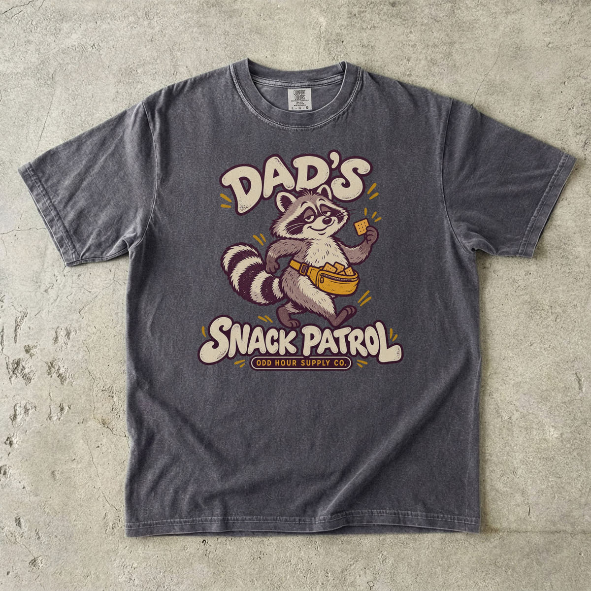 Pepper Comfort Colors 1717 T-shirt with a raccoon, a yellow waist pack full of crackers, and cream Dad’s Snack Patrol lettering.