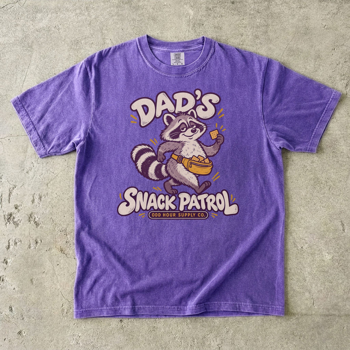Violet Comfort Colors 1717 T-shirt with a raccoon, a yellow waist pack full of crackers, and cream Dad’s Snack Patrol lettering.