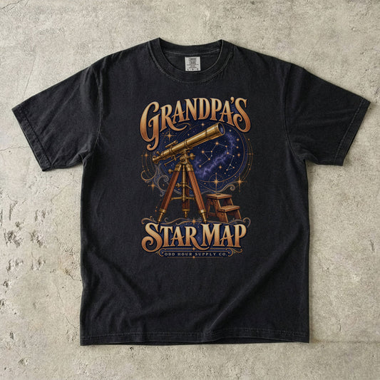 Black T-shirt with GRANDPA’S STAR MAP, a brass telescope, a starry sky and a small stool by Odd Hour Supply Co.