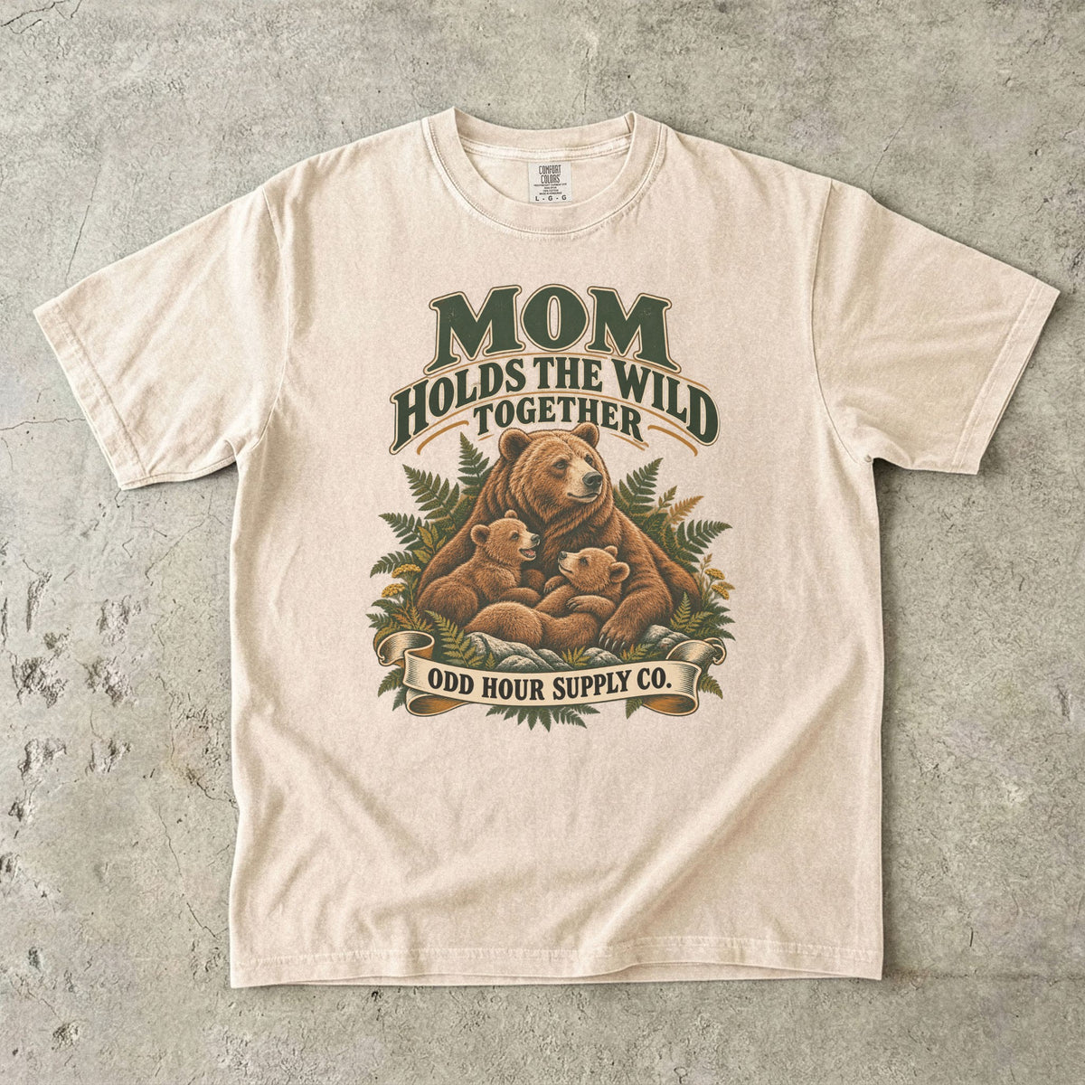 Ivory Comfort Colors 1717 T-shirt with a mother bear, two cubs, ferns, and Mom Holds the Wild Together lettering.