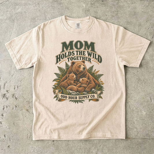 Ivory Comfort Colors 1717 T-shirt with a mother bear, two cubs, ferns, and Mom Holds the Wild Together lettering.