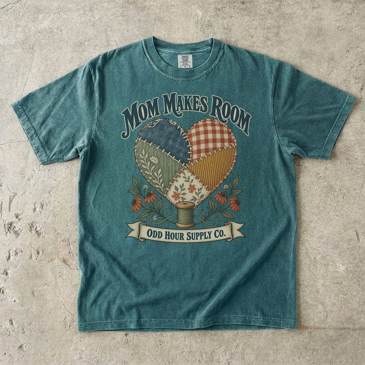 Blue Spruce Comfort Colors 1717 T-shirt with a heart made of patterned fabric patches, flowers, a spool of thread, and Mom Makes Room lettering.
