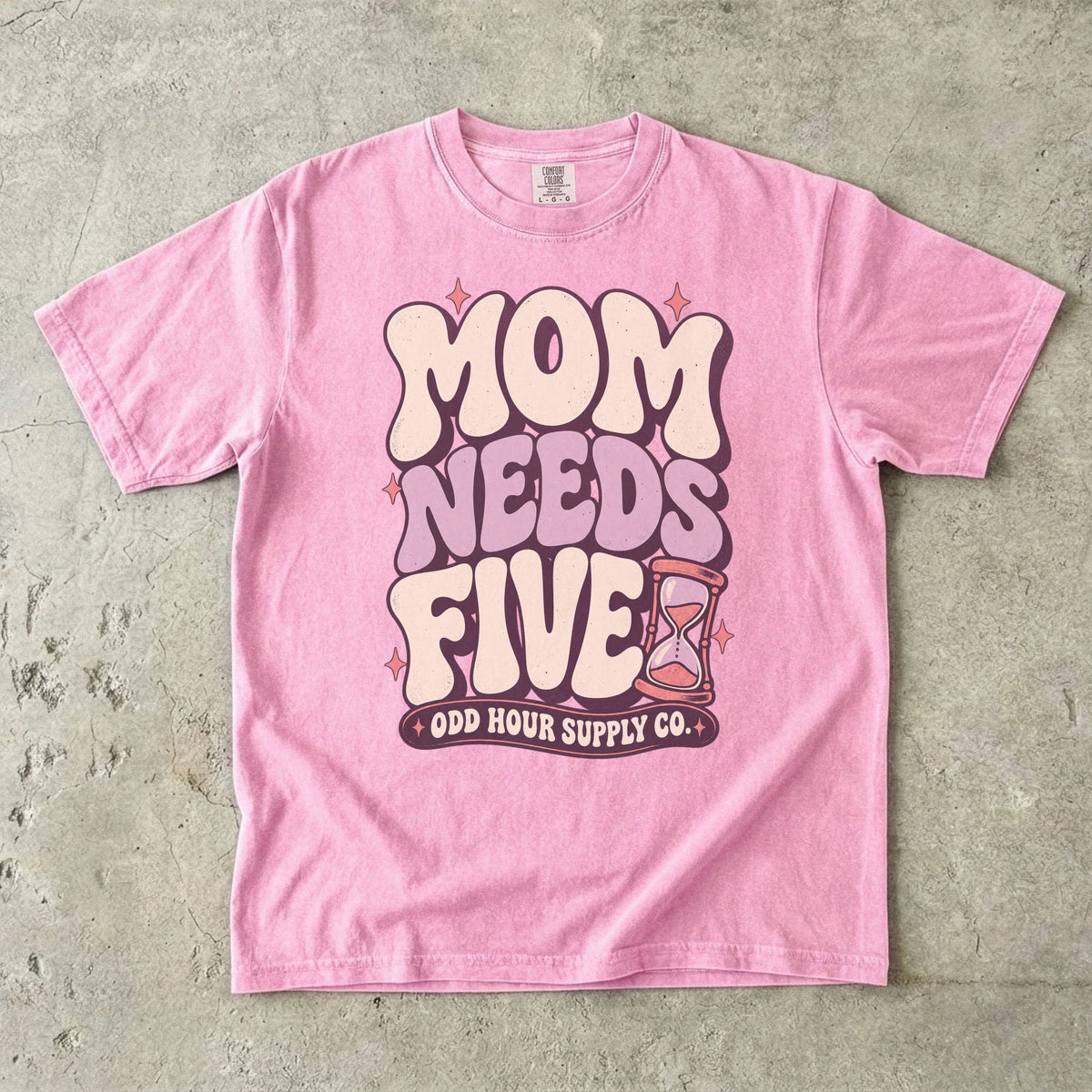 Blossom Comfort Colors 1717 T-shirt with cream and lilac Mom Needs Five lettering, pink stars, and an hourglass.