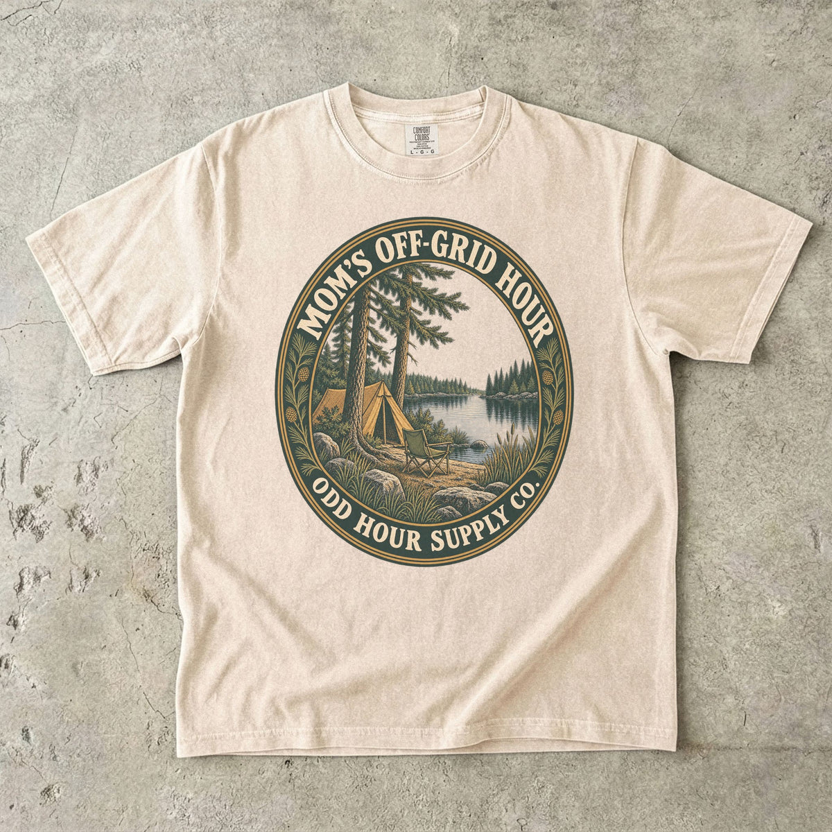 Ivory Comfort Colors 1717 T-shirt with an oval Mom’s Off-Grid Hour badge showing a tent, a camp chair, pine trees, and a lake.