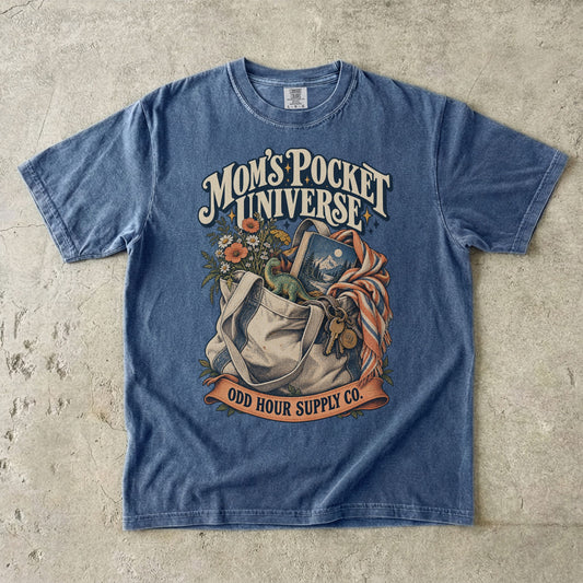 Denim Comfort Colors 1717 T-shirt with a tote bag holding flowers, a book, a toy dinosaur, and keys beneath Mom’s Pocket Universe lettering.
