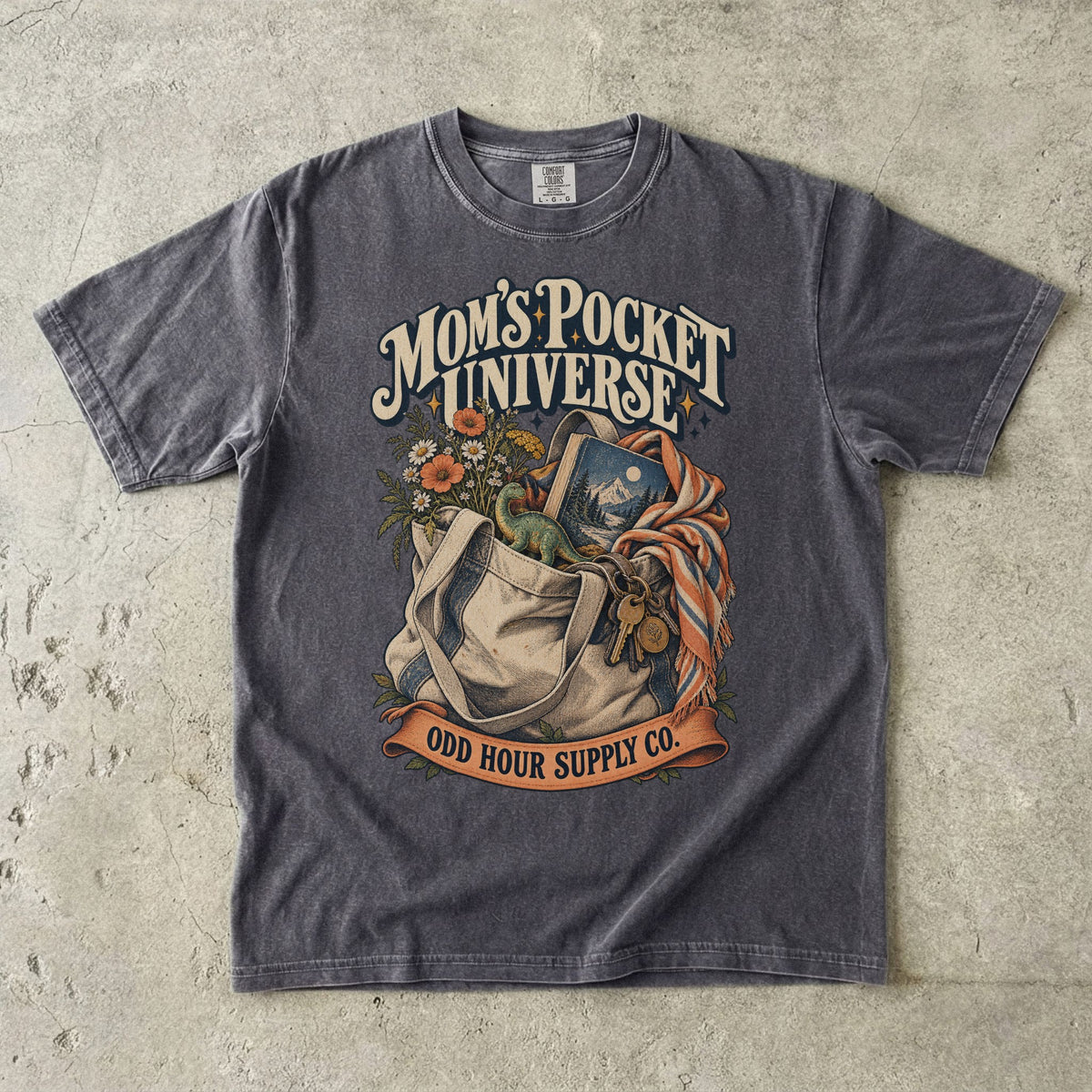 Pepper Comfort Colors 1717 T-shirt with a tote bag holding flowers, a book, a toy dinosaur, and keys beneath Mom’s Pocket Universe lettering.