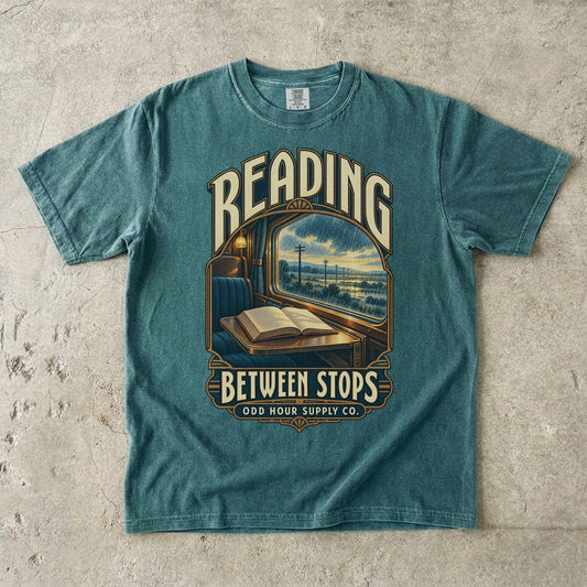 Blue Spruce T-shirt with a train window, open book and READING BETWEEN STOPS by Odd Hour Supply Co.