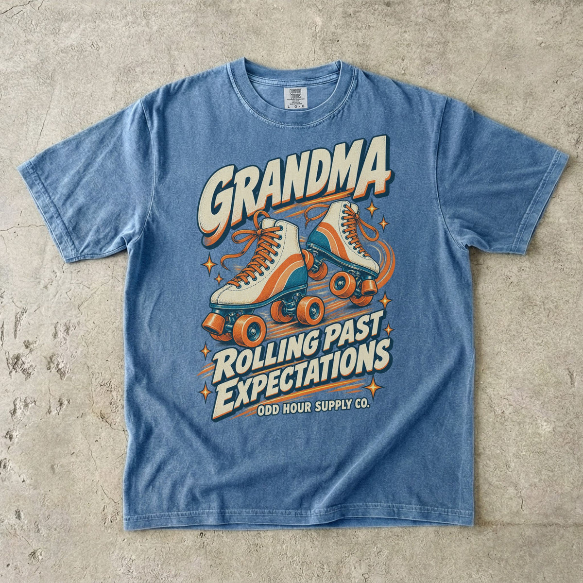 Blue Jean Comfort Colors 1717 T-shirt with cream roller skates, orange and teal details, and Grandma Rolling Past Expectations lettering.