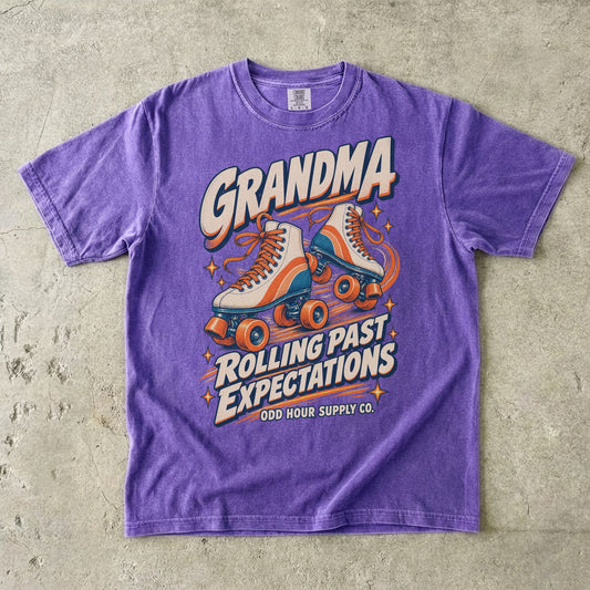 Violet Comfort Colors 1717 T-shirt with cream roller skates, orange and teal details, and Grandma Rolling Past Expectations lettering.
