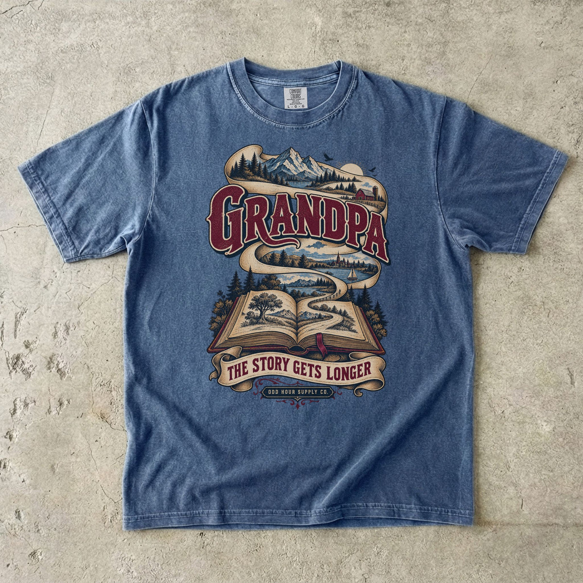 Denim T-shirt with GRANDPA THE STORY GETS LONGER, an open book and a landscape ribbon by Odd Hour Supply Co.