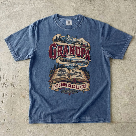 Denim T-shirt with GRANDPA THE STORY GETS LONGER, an open book and a landscape ribbon by Odd Hour Supply Co.