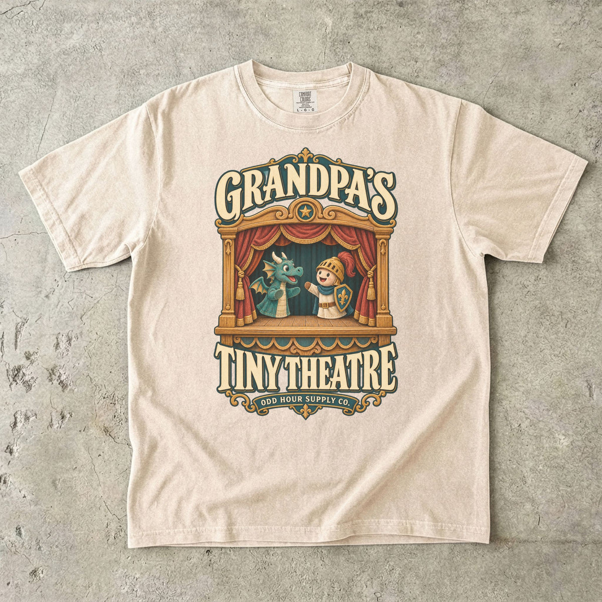 Ivory T-shirt with GRANDPA’S TINY THEATRE, a wooden puppet theatre, red curtains, a dragon and a knight by Odd Hour Supply Co.