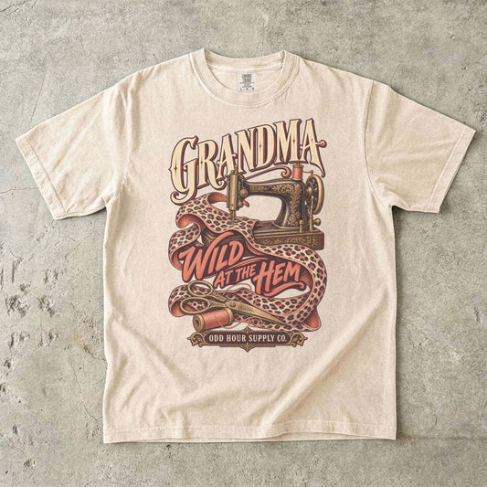 Ivory Comfort Colors 1717 T-shirt with an ornate sewing machine, leopard-print fabric, thread spools, and Grandma Wild at the Hem lettering.