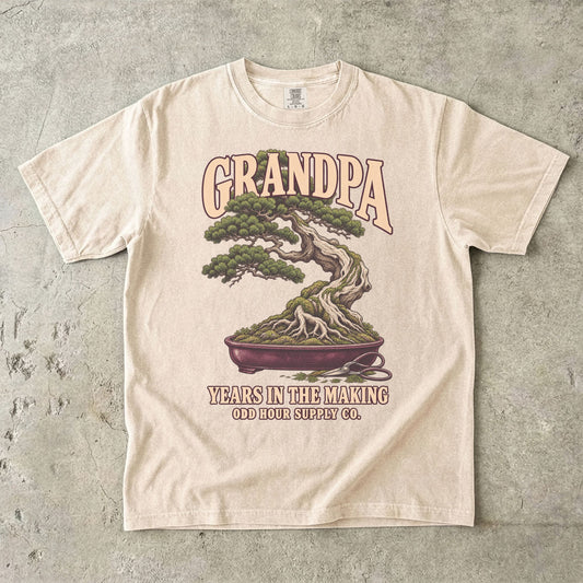 Ivory T-shirt with GRANDPA YEARS IN THE MAKING, a bonsai tree, exposed roots and small pruning shears by Odd Hour Supply Co.